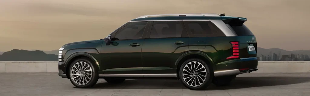 The image shows a side view of the 2026 Hyundai Palisade Hybrid. The sleek and modern SUV features stylish wheels, a two-tone exterior, and a spacious design perfect for road trips.