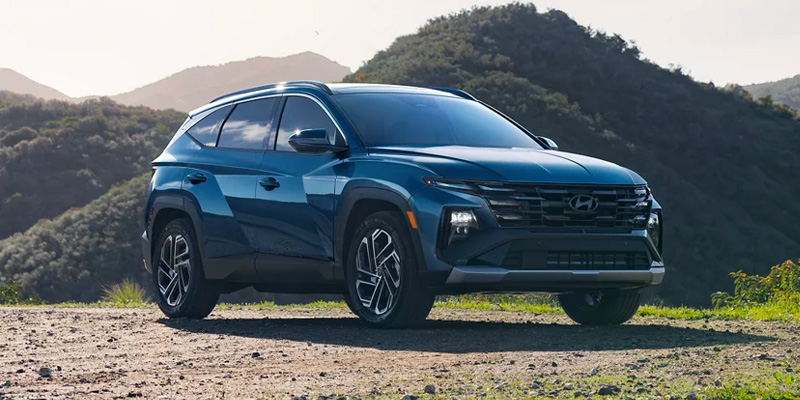 Blue Hyundai Tucson SUV parked on a scenic mountain overlook with hills in the background.