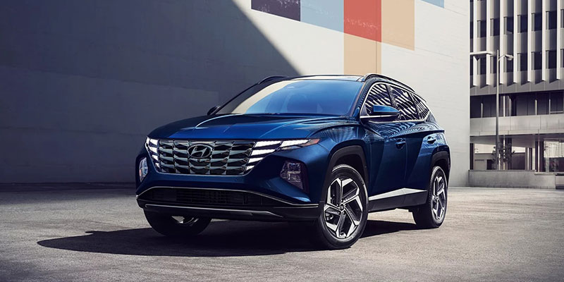 A blue Hyundai SUV parked in an urban setting with a modern building in the background.
