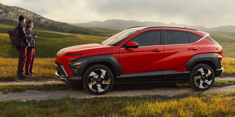 Couple standing in front of Hyundai Kona parked on lush mountain road.