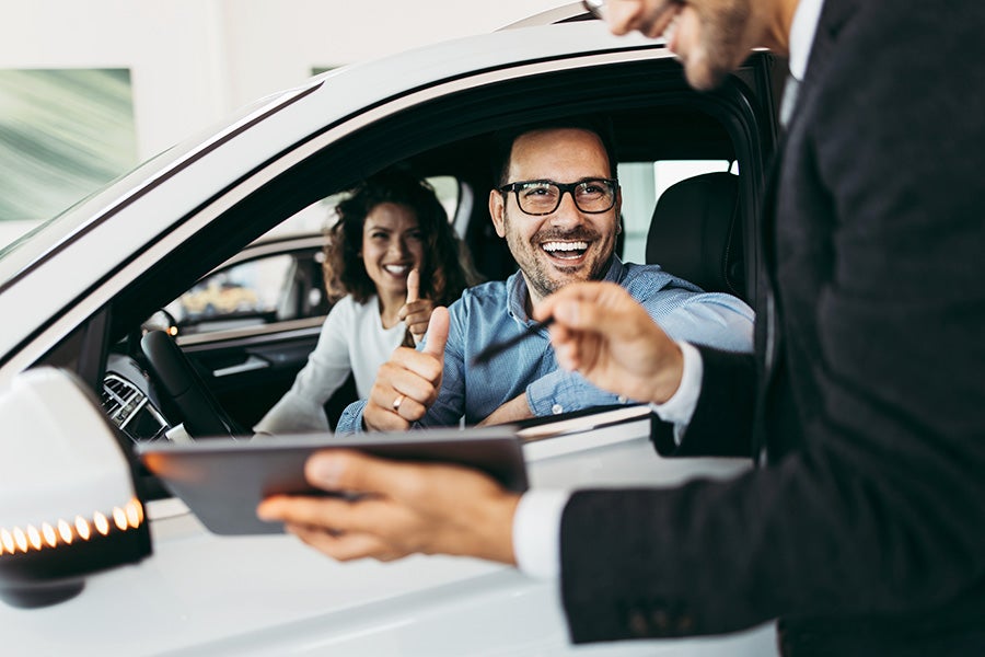 Photo of two happy people in a car interacting with a car sales specialist